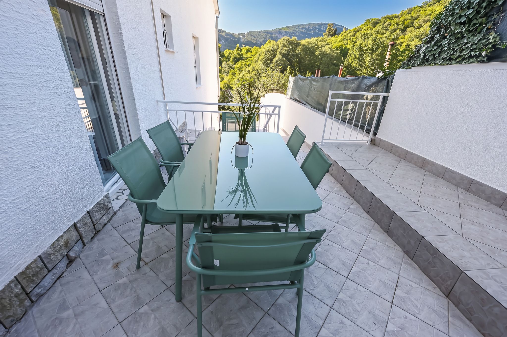 The walled terrace of the two-bedroom, with a glass table and green chairs